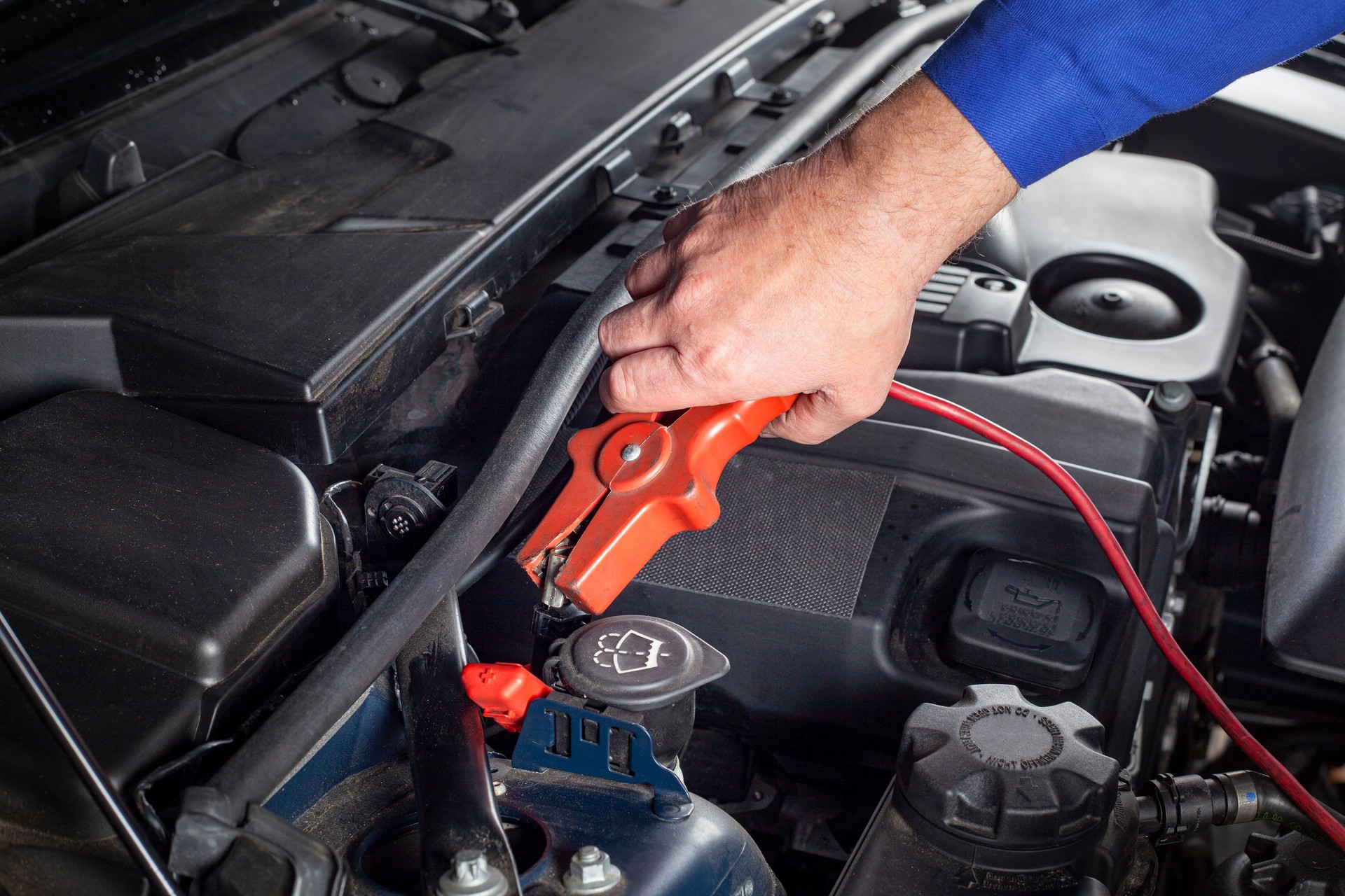 Mechanic is connecting a booster-cable to the battery in order to jump-start a car